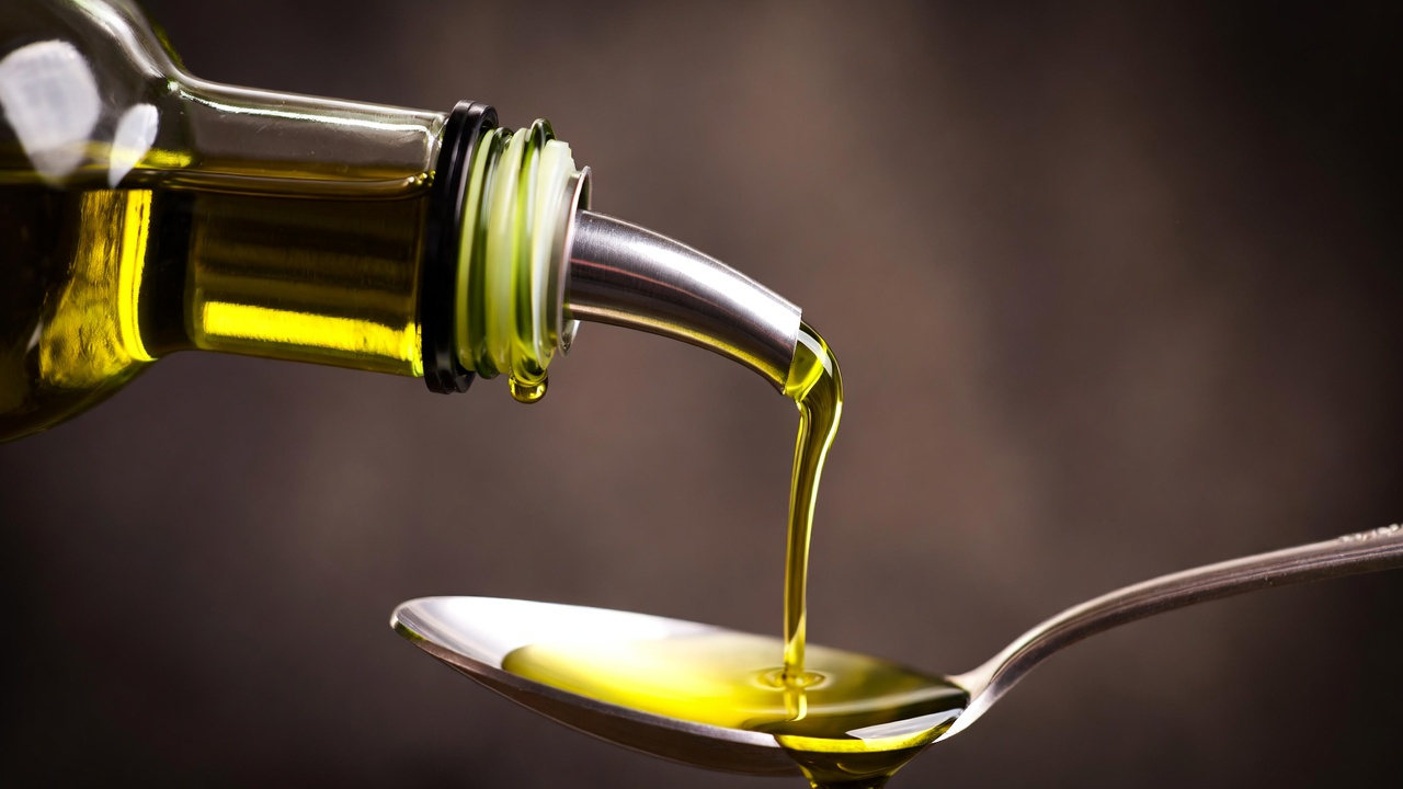 Extra-virgin olive oil being poured from a bottle onto a tablespoon — illustrating a single measured serving